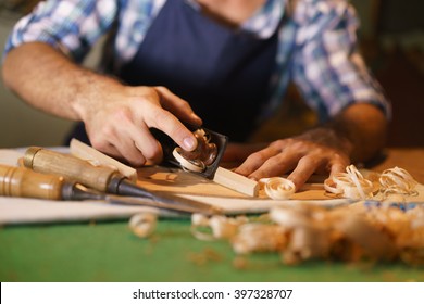 Lute maker shop and acoustic music instruments: young adult artisan cutting and chiseling wood to make a classic guitar. Closeup of his hand using a tool on guitar body