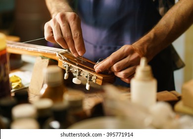 Lute Maker Shop And Classic Music Instruments: Young Adult Artisan Fixing Old Classic Guitar Adding A Cord And Tuning The Instrument. Close Up Of Hands And Palette