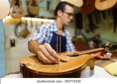 Lute Maker Shop And Classic Music Instruments: Young Adult Artisan Fixing Old Classic Guitar, Tuning The Instrument With A Metallic Diapason. Closeup Of Hand On Guitar Body