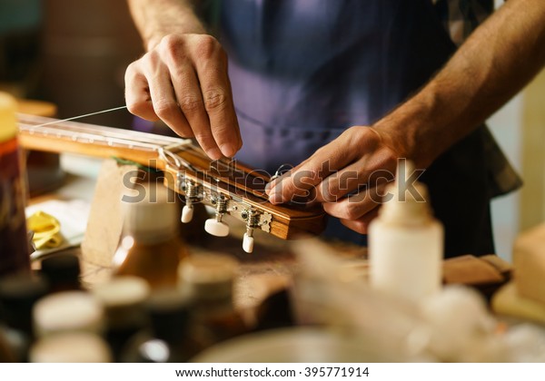 Lute maker shop and classic
music instruments: young adult artisan fixing old classic guitar
adding a cord and tuning the instrument. Close up of hands and
palette