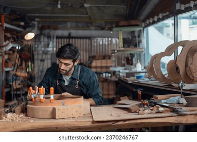 Luthier creating a guitar and using tools in a traditional, clamps on the body of a guitar under construction improving glue adhesion