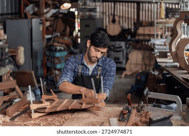 Luthier creating a guitar and using tools in a traditional, clamps on the body of a guitar under construction improving glue adhesion.