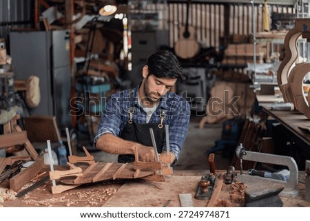 Luthier creating a guitar and using tools in a traditional, clamps on the body of a guitar under construction improving glue adhesion.