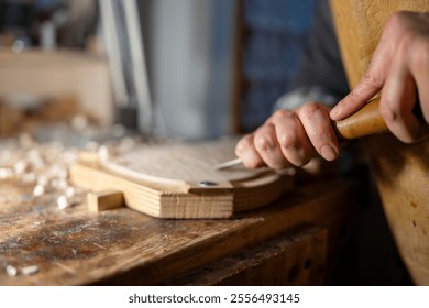 Luthier meticulously carves a piece of wood, using a gouge, in a traditional workshop, surrounded by wood shavings