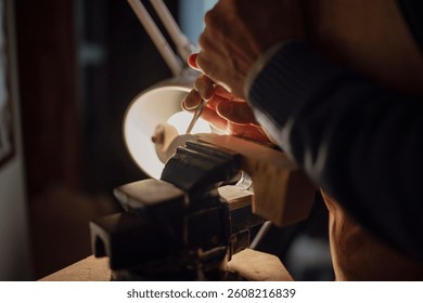 Luthier meticulously carves a piece of wood, clamped in a vise, using a gouge, under the warm glow of a lamp, showcasing the craftsmanship involved in creating musical instruments