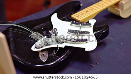 Luthier unscrewing pickguard and shows electrical components of guitar
