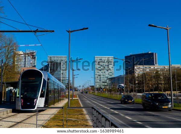 Luxembourg-City,\
Luxembourg - February 8, 2020 - and tram street car train at a halt\
at a railway stop on Kirchberg in front of business district\
skyscrapers and European\
institutions
