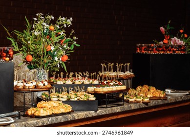 Luxurious appetizer display featuring mini sandwiches, canapes, and shrimp bites on tiered stands, accented by a fresh floral-and-orange centerpiece