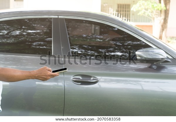 A luxurious car owner is using a\
smartphone to lock, unlock and start car engine, a photo of\
selective focus with concept of high technology operated\
car.