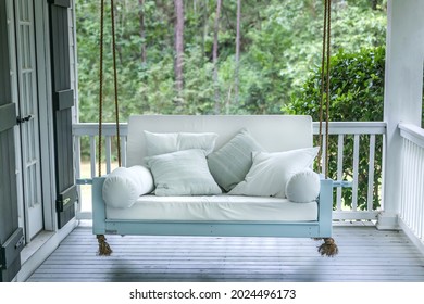 A luxurious and classic outdoor bed swing painted a seafoam green with white deep cushions and the swing is hung from the ceiling by rope. - Shutterstock ID 2024496173