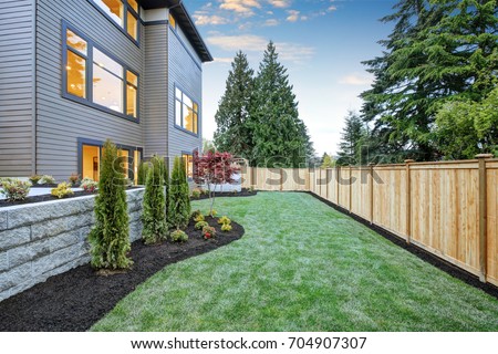 Luxurious contemporary three-story wood siding home exterior in Bellevue. Nice backyard landscape with well kept lawn, flower beds and wooden fence. Northwest, USA
