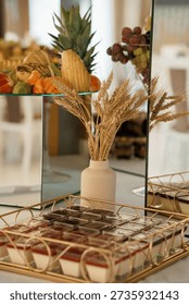 A luxurious dessert table setup featuring an array of fresh fruits, chocolate treats, and decorative wheat stalks, ideal for weddings, parties, or upscale events with a rustic-chic aesthetic