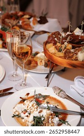 Luxurious dining setup featuring a variety of gourmet cheeses, fruits, and nuts on a wooden platter. Accompanied by two glasses of white wine creating an elegant dining experience.