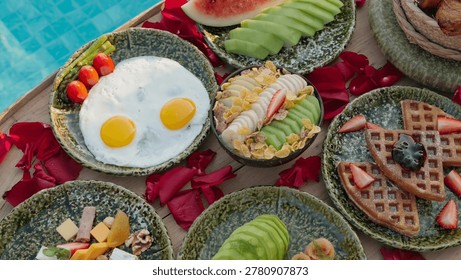 A luxurious floating breakfast spread featuring eggs, waffles, fruits, and rose petals by a blue swimming pool