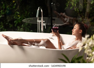 A Luxurious Girl Is Relaxing In A Bubble Bath With A Glass Of Wine. Spa And Relaxation