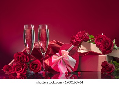 Luxurious glasses with sparkling wine open box with glitter brocade and gift box in the shape of a heart surrounded by selected roses on a mirror surface on a red background. Valentine's day - Powered by Shutterstock