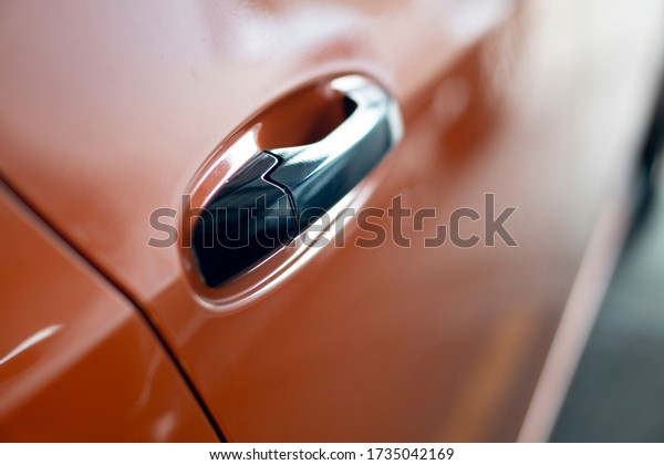 Luxurious handle of door car chrome color. with\
blurred orange doors.
