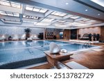 A luxurious indoor swimming pool area in a high-end resort or hotel, featuring a spacious and elegant design. The pool is surrounded by comfortable lounge chairs, tropical plants, and modern lighting