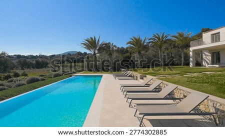 Luxurious infinity pool lined with comfortable sun loungers, overlooking a lush valley with palm trees under a vast, cloudless blue sky