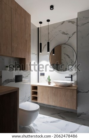 Luxurious interior of bathroom with marble on the floor and wall. Round mirror and stylish modern bathroom sink.