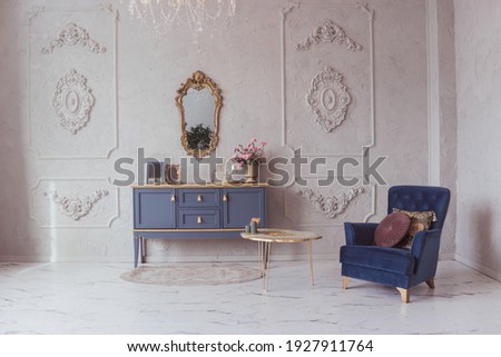Luxurious interior with a chest of drawers and velvet armchair in a classic style, marble floor, stucco decor on the walls