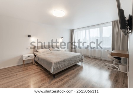 Luxurious master home bedroom interior, modern house, beautiful interiors, wide bedroom. TV Set on the Wall. King Size Bed, White Walls and Ceiling. Hardwood Floor. Wide Angle