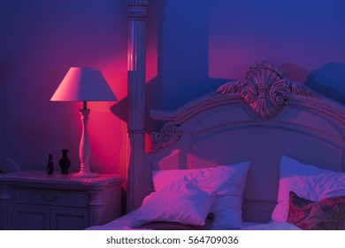 Luxurious Minimalistic Art Décor Bedroom With Royal Bed, Pink And Blue Light With Stylish Night Lamp At The Wooden Table 