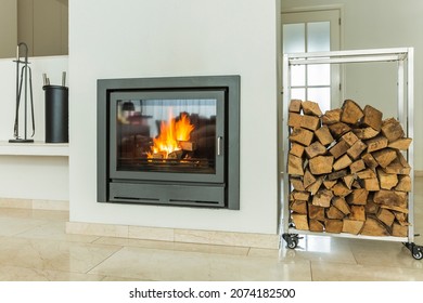 Luxurious modern design fireplace burning firewood, door with fire resistant glass window. Home interior with white walls on yellow marble floor