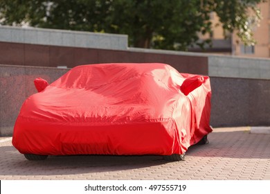 luxurious red roadster in cover protects against rain of dust and dirt