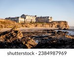 A luxurious resort and spa hotel on the Pacific Ocean Coastline and the public Coastal Trail at sunset seen from the beach at low tide, located on a golf course. Half Moon Bay hotel on the cliff