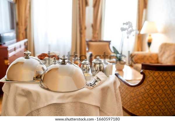 Luxurious Room Service. Breakfast in\
luxury hotel room delivered by waiter. Meals under silver cloche.\
Hospitality and vacation concept. Horizontal\
shot