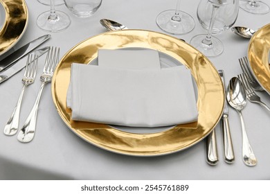 Luxurious table setting featuring gold charger plates, silverware, and a folded white napkin. Perfect for weddings, fine dining, and formal events, showcasing elegance and sophistication. - Powered by Shutterstock