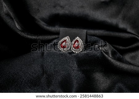 Luxurious teardrop-shaped ruby earrings surrounded by diamonds, displayed on rich black satin fabric. The contrast enhances the jewelry’s elegance and sophistication