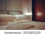 Luxurious and warmly lit hotel room, creating an inviting and cozy atmosphere. The room is furnished with a large, plush bed dressed in soft white linens, complemented by a stylish padded headboard. 