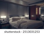 Luxurious and warmly lit hotel room, creating an inviting and cozy atmosphere. The room is furnished with a large, plush bed dressed in soft white linens, complemented by a stylish padded headboard. 