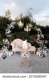 Luxurious wedding setup featuring a beige chaise lounge beneath a floral arch with chandeliers, creating a romantic outdoor ambiance