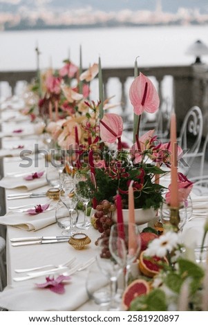 A luxurious wedding table setup overlooking the serene waters of Lake Como. The design features vibrant pink anthuriums, tropical fruits such as grapefruits,
