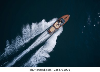 Luxurious wooden boat fast movement on dark water. Classic Italian wooden boat fast moving aerial view. Top view of a wooden powerful motor boat. Large expensive varnished wooden boat top view