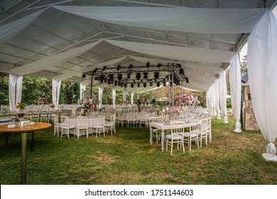 A luxury alfresco wedding reception set up at the countryside; white rustic tiffany chairs, top table flower arrangements, crystal center pieces, lights and music system.