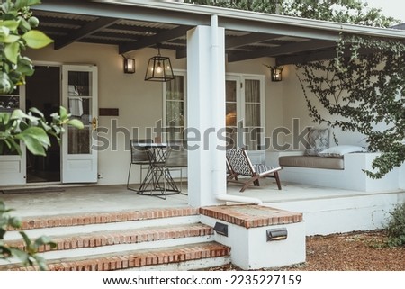 The luxury allure of a South African cottage. The charm of modern furnishings, greeted by elegant French doors and a veranda surrounded by lush overgrown plants. A modern and cozy outdoor living. 