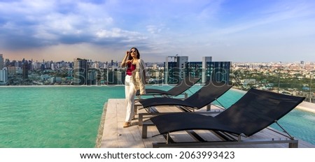 Luxury Asian CEO woman entrepreneur standing on the rooftop swimming pool looking to the sun with skyscraper and cityscape on the background