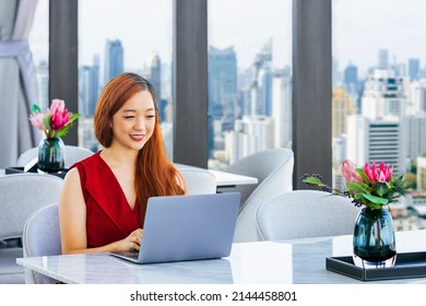 Luxury Asian Millionaire CEO In Red Dress Is Working With Laptop Computer In The Prestige Classy Office With Skyscraper View For Wealthy And Upper Class Lifestyle