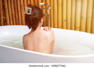 Luxury bath asia woman wellness spa relaxing soaking in warm water bathtub of hotel suite. back view.