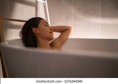 Luxury bath woman relaxing in hotel spa bathtub or home bathroom for total relaxation. Asian lady taking a bath sleeping in warm water, winter wellness.