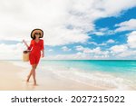 Luxury beach travel vacation elegant lady walking relaxing on holidays with beachwear accessories sunglasses, sun hat and bag wearing red cover-up dress.