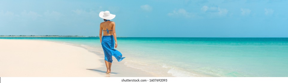 Luxury beach vacation elegant tourist woman walking relaxing in beachwear hat on white sand Caribbean beach. Lady tourist on holiday vacation resort. Banner panorama landscape.
