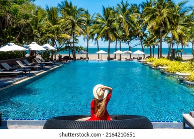 Luxury beach vacation in tropical beach hotel. Tourist woman in red dress relax near blue swimming pool in modern resort. Female traveler on sea vacation. - Powered by Shutterstock