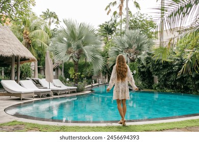 Luxury beach vacation in tropical beach hotel. Tourist woman wearing dress relax near blue swimming pool in modern resort. Female traveler on sea vacation. - Powered by Shutterstock