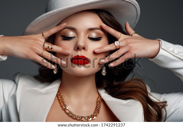 Luxury beautiful fashionable confident woman\
wearing stylish accessories: a lot of golden rings, chunky chain,\
earrings, hat. Female fashion, beauty, advertising concept. Close\
up studio portrait