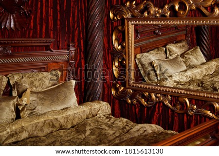 Luxury bedroom in medieval style with art Deco elements and large mirror. Bed and items with patterns. Refined interior. Comfortable king size bed in gold color. Copyright space for website or banner
